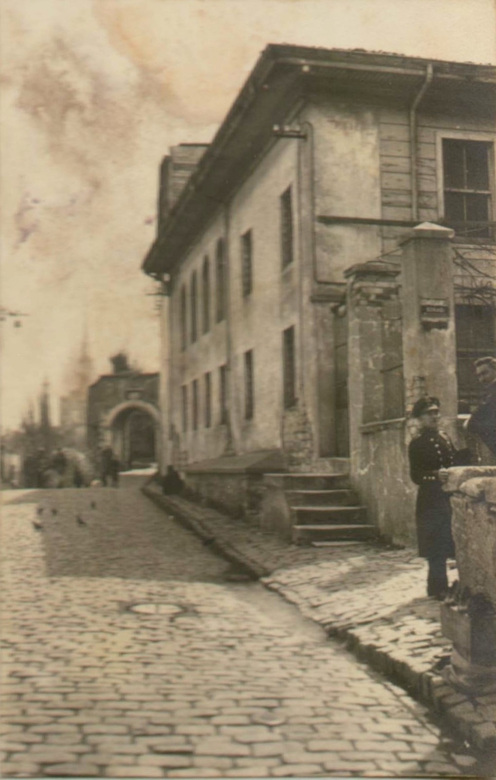 Dergâh girişi. Arnavutkaldırımlı sokakta bir Osmanlı muhafızı; arka planda cümle kapısı seçiliyor.