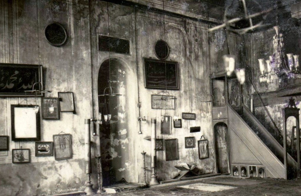 Mihrap duvarı; çevresini saran hat levhaları, mihrabın yanlarında madenî şamdanlar, sağda ahşap minber.